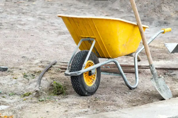 Photo of Wheelbarrow. ld yellow Trolley for construction. Using feathers, stones, sand, cement.