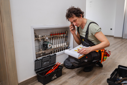 Repairmen calling colleague for advice about a problem with underfloor heating pipes