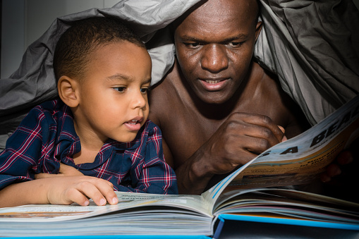 Father reading a book for his son under the blanket