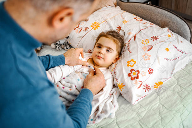 istock Father measuring his daughters body temperature with thermometer while she is lying in bed wrapped in warm blanket 1465567824