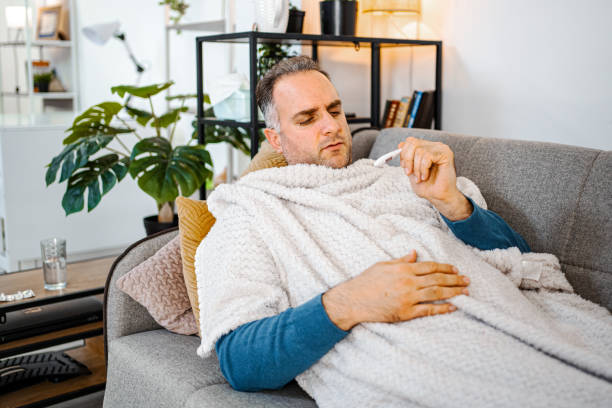 istock Men measuring his body temperature with thermometer while lying in bed wrapped in warm blanket 1465567895