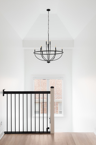 A hallway and staircase with a wrought iron railing, hardwood floor, and chandelier hanging from the tall ceiling.