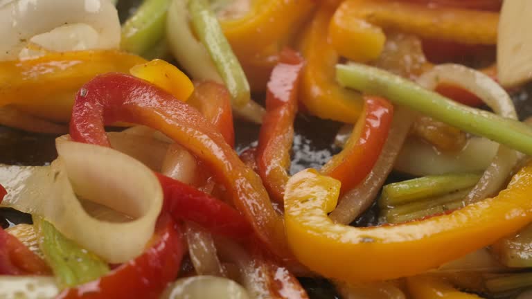 Super close-up of the red and yellow peppers and onion stir-frying on the pan