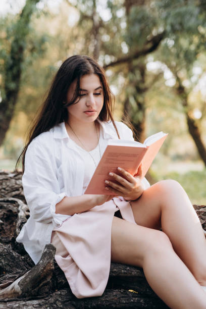 istock young girl in white clothes sits on a tree in the forest 1465570883