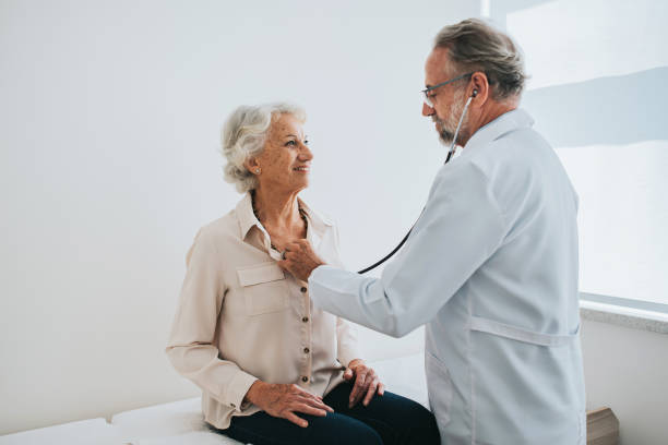 Doctor listening to senior woman patient heartbeat stock photo
