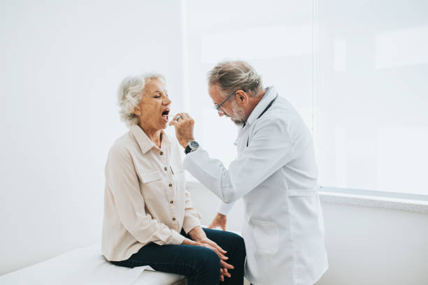 patient âgé avec un mal de gorge par piqûre de langue - doctor patient male tongue depressor photos et images de collection