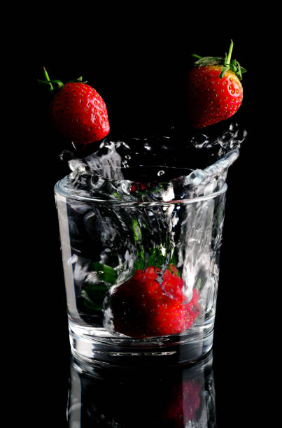 strawberries are splashing in a glass of water stock photo
