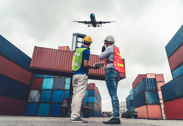 istock Industrial worker works with co-worker at overseas shipping container port . Logistics supply chain management and international goods export concept . 1465575700