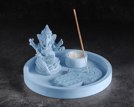 Set of gypsum products for meditation, relaxation, aromatherapy. Ganesh figurine, aroma stick on a stand, candlestick with a tealight on a tray, low key, selective focus.