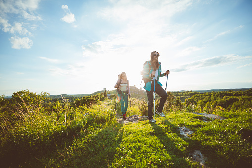 Two young women wearing sports clothes and backpacks hiking the hills at sunset.