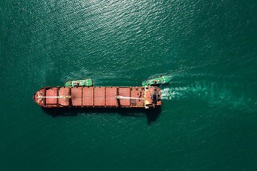 aerial top view tugboat pulling red oil ship to shipyard dry dock repairing and maintenance in green sea