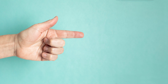 closeup view of a caucasian person's hand pointing with the finger to the copy space, on light blue background