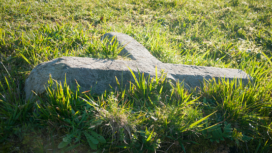 Broken stone cross in green grass field