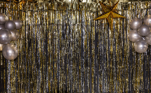 Copy space shot of a gold and silver colored sparkly tinsel curtain backdrop for New Year's eve party celebration decorated with a gold colored star and balloons.