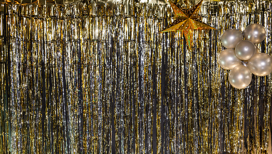 Copy space shot of a gold and silver colored sparkly tinsel curtain backdrop for New Year's eve party celebration decorated with a gold colored star and balloons.