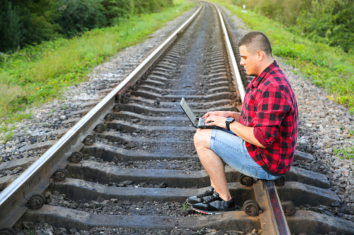 Guy with a laptop is sitting on the railway tracks.