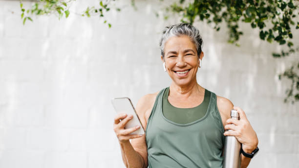 mujer mayor motivada navegando por algo de música para su rutina de ejercicios al aire libre - senior adult happiness lifestyles cheerful fotografías e imágenes de stock