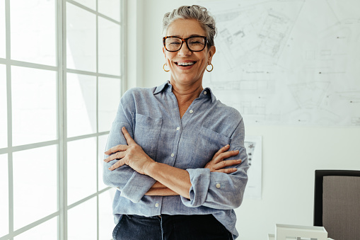 Successful senior business woman standing in her office and looking at the camera with a smile. In portrait, this mature design architect shows pride in her skills as an experienced professional.