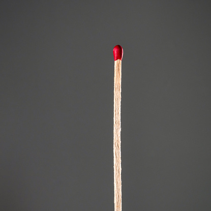Close-up image of an unlit match, against a grey background.