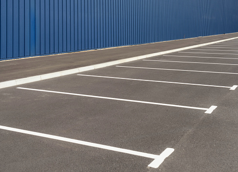 A long row of curbside parking spaces in a large parking lot outside an industrial building.