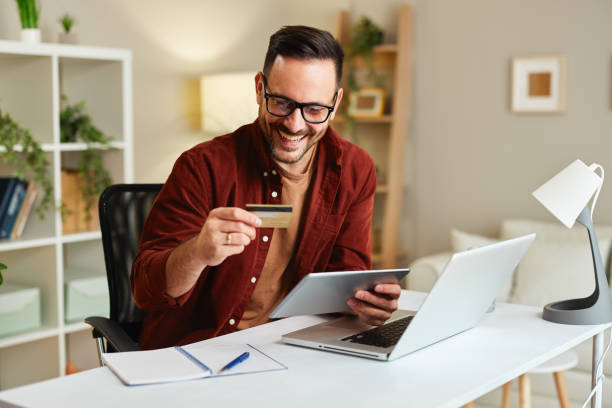 istock Young man holding credit card and tablet at home at table 1465592746