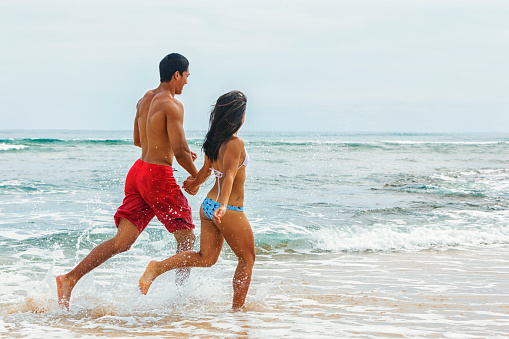 Photo of a young physically fit Hawaiian couple running on the beach