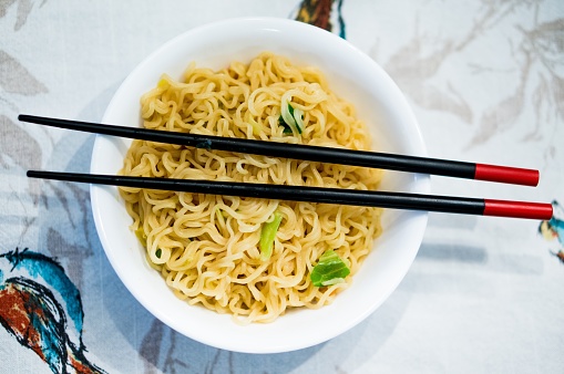 a bowl of fried noodles on the dining table with black chopsticks in the bowl