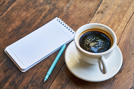 a cup of warm coffee, a notebook and a blue pen on the desk