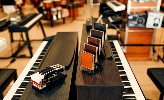 Close-up of black pianos with wood color samples in a musical instrument store. Lots of different keyboard instruments for sale. Hobbies and recreation.
