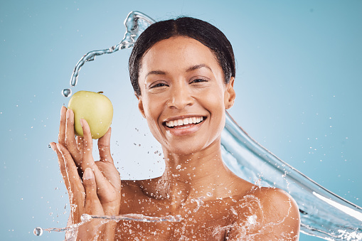 Water, apple and beauty with black woman and splash from shower for cleaning, hygiene and skincare with vegan, healthy and wellness cosmetics. Fruit, water splash and cosmetic portrait and mock up.