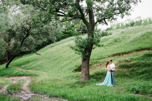 happy guy in a white shirt and a girl in a turquoise dress, the bride and groom are walking in the forest park