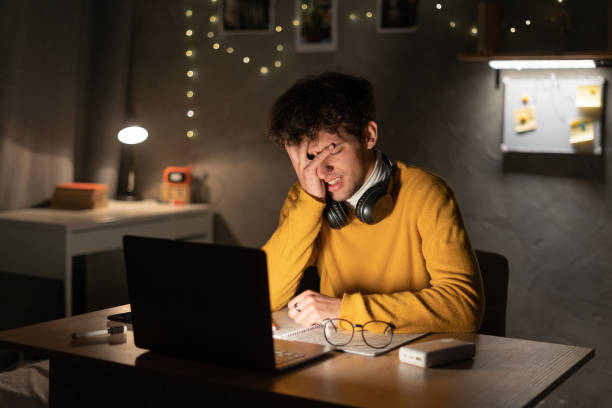 unavený vyčerpaný arabský muž, vysokoškolský student na koleji nebo na volné noze, sedící u svého stolu, unavený studiem v notebooku, přepracovaný, má bolesti hlavy, potřebuje odpočinek a přestávku v noci - bolest-hlavy-ilustrace - stock snímky, obrázky a fotky