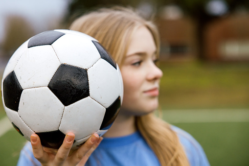 A confident Caucasian female soccer player stands for a portrait at a team practice game.