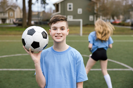 A coed soccer team practice game consisting of boys and girls on the field.  One of the players stands for a portrait. Shot in Portland, Oregon, USA.
