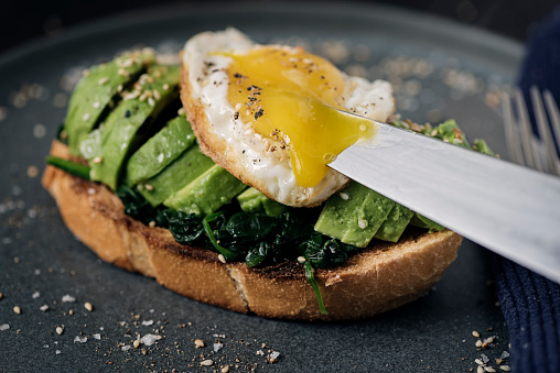 Avocado toast with spinach, fried egg and toasted sesame seeds. Colour, horizontal format with some copy space.