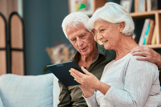 老人、夫婦、タブレットと高齢者がオンラインで閲覧し、絆を深めながらソーシャルメディアでコンテンツを検索します。引退した男性と女性のスクロールメディアとの接続、デジタルデバ� - senior adult couple computer retirement ストックフォトと画像
