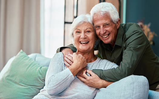 Portrait, hug and senior couple in living room in home, smiling and bonding. Love, retirement and smile of happy elderly man and woman on sofa, embrace and enjoying quality time together in house.
