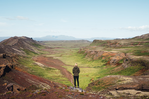 Woman standing on top of the hill enjoying the view on dramatic and colorful volcanic landscape in Iceland (Dyradalur).