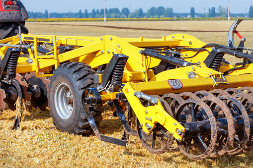 A powerful multi-row disc harrow as a trailer to a tractor for tillage against the backdrop of an agricultural field on a summer day.