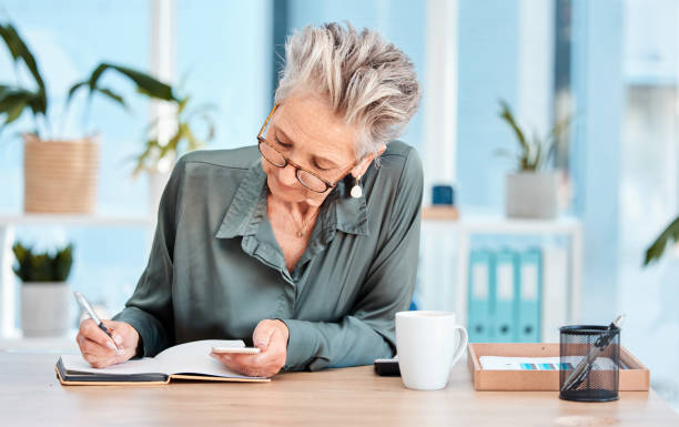 istock Writing, notebook and schedule with a woman ceo, manager or boss checking her diary for an appointment. Calendar, coffee and notes with a senior female employee using a pen to write in her planner 1465611003