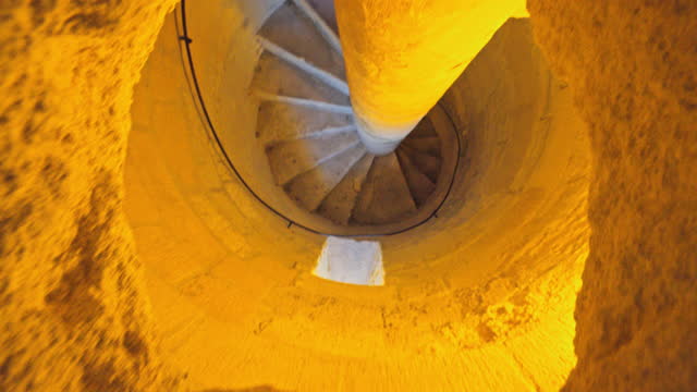 View from above illuminated spiral staircase in stone hole