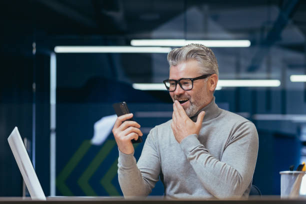 istock Mature businessman with beard using app on phone inside office, man received online message notification about good news, boss texting online at workplace 1465614278