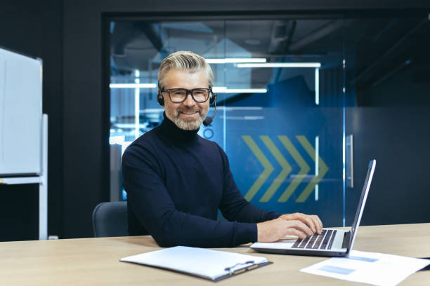 istock A gray-haired handsome businessman with a headset and a microphone is working on a laptop 1465614427