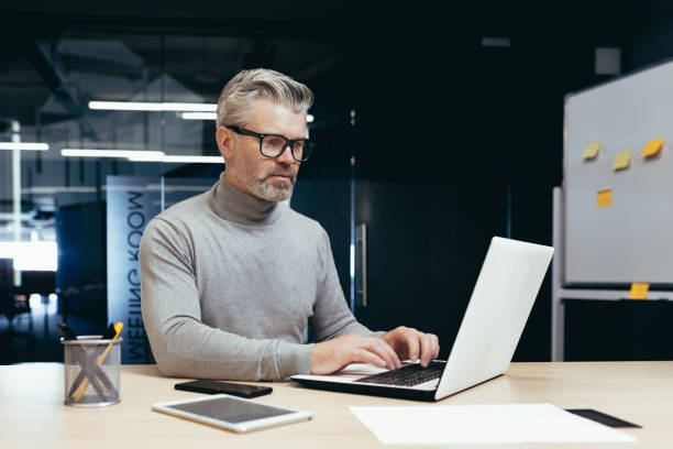 istock A senior gray-haired man, financial analyst, is working in the office at a table with a laptop 1465614448