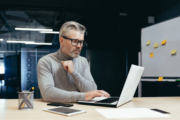 istock Concentrated senior gray-haired male designer, engineer, architect works in the office at a laptop 1465614529