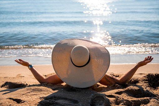 Close up rear view on female with big sun hat while looking at sea view from the sand beach. Woman relaxing on summer vacation. Copy space