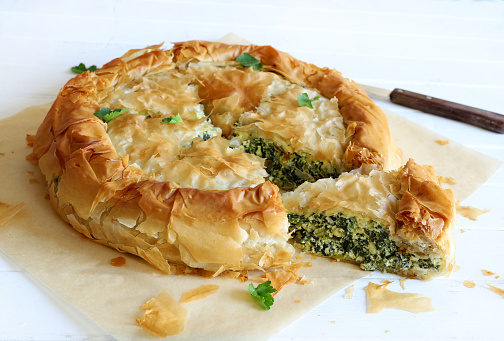 Traditional Greek cuisine. Spanakopita, savory pie. Homemade Greek phyllo dough pie filled with spinach and feta cheese on white background.