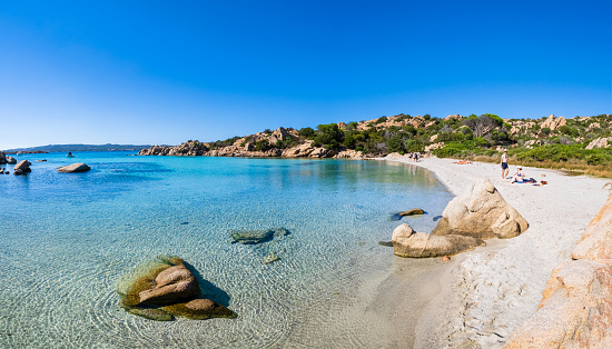 Tourists enjoying a beautiful sunny October day at the Cala Serena, one of the beautiful beaches in Caprera, island of the Maddalena Archipelago (4 shots stitched)