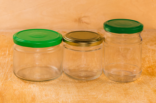 Empty small glass jars different sizes closed with screw colored lids on a wooden surface