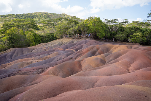 The Seven Coloured Earths are a geological formation of sand dunes, each of which is a different color: red, brown, purple, green, blue, purple and yellow. The different colors are caused by the presence of different minerals in the soil. The sand dunes are surrounded by lush green vegetation and are a popular tourist attraction. The Seven Coloured Earths are located in a secluded and peaceful area, providing a perfect spot for those looking to escape the hustle and bustle of everyday life. The overall scene is one of natural beauty and tranquility, showcasing the unique and breathtaking landscapes that can be found in this part of the world. The image captures the beauty and the contrast of the colorful earths, creating an amazing and unique sight.